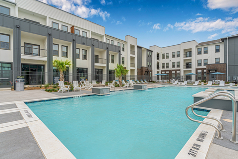 A swimming pool in front of a building with lounge chairs around it.