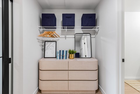 A small kitchen with a white fridge, a beige drawer, and a shelf with bags and a plant.