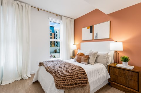 A bedroom with a large bed and a window with white curtains.
