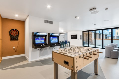 A foosball table is in the middle of a room with two TVs on the wall.