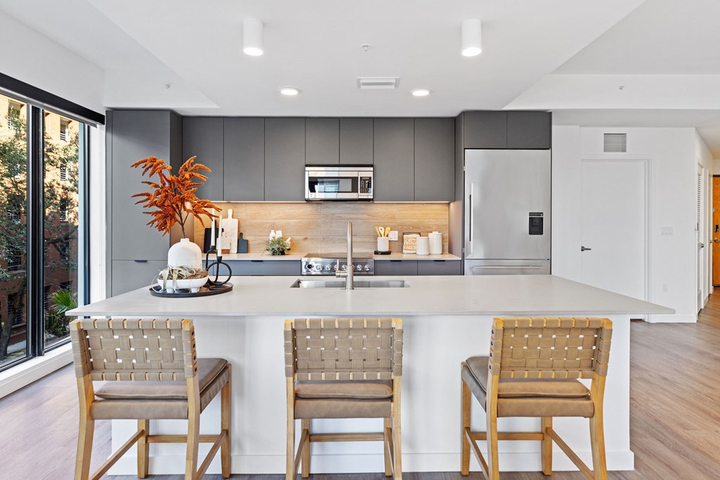 A modern kitchen with a white island and wooden chairs.