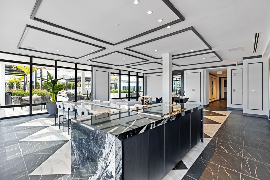 A black reception desk with a marble top sits in a spacious lobby with a view of the outdoors.