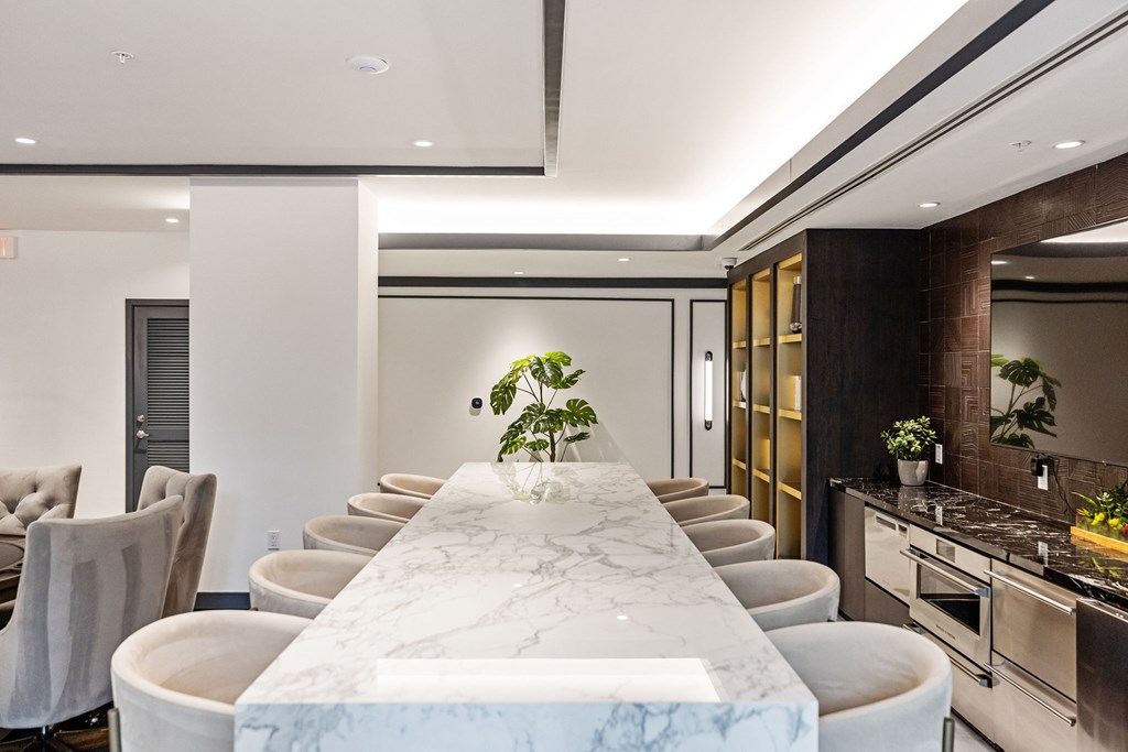 A long marble table with chairs on either side is in the middle of a room.