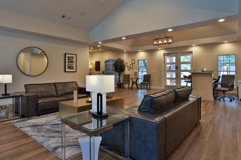 A modern living room with a glass coffee table and dark brown leather couches.