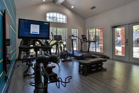 A gym with exercise equipment and a television displaying a webpage at The Quarry Alamo Heights Apartments, Texas, 78209