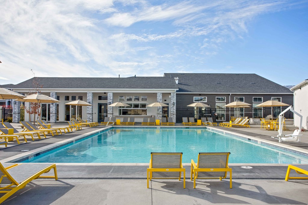 a swimming pool with yellow chairs and a building in the background