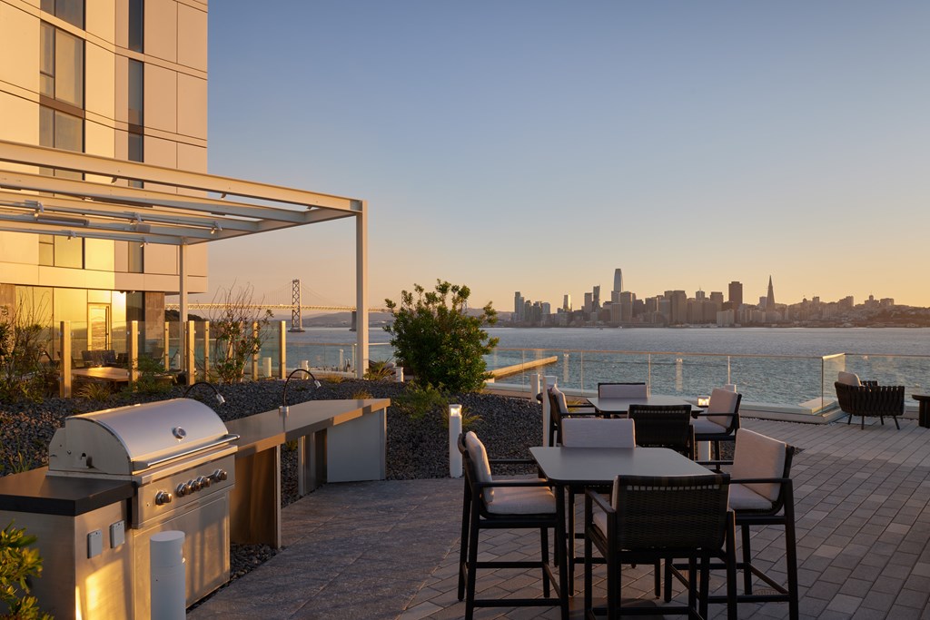 A patio with a table and chairs overlooking a city skyline at dusk.
