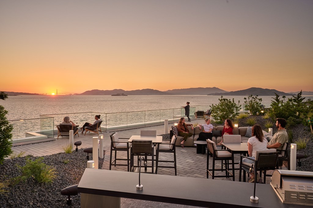 a group of people sitting on a patio overlooking the water at sunset