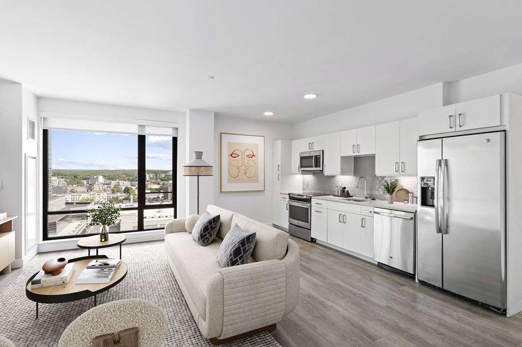 a living room with a white couch and a white kitchen with stainless steel appliances