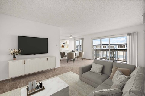 A living room with a flat screen TV, a white cabinet, a grey sofa, a coffee table, and a dining table with chairs.