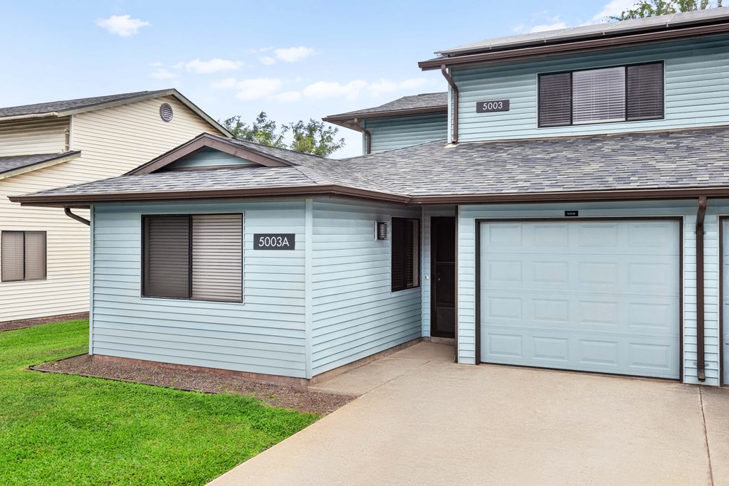exterior shot of home. Driveway and garage. Blue paint. small front yard with grass.