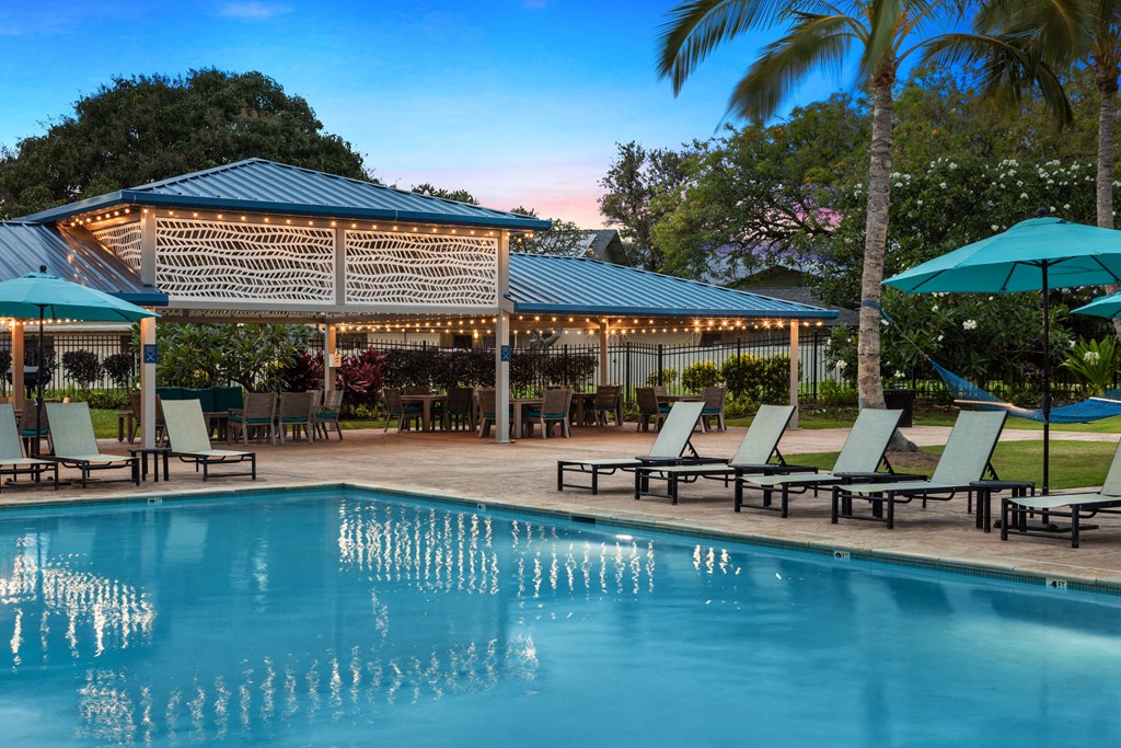 pool area showing covered bbq area. Seating with tables. Lounge furniture around pool. Sunset in the background.