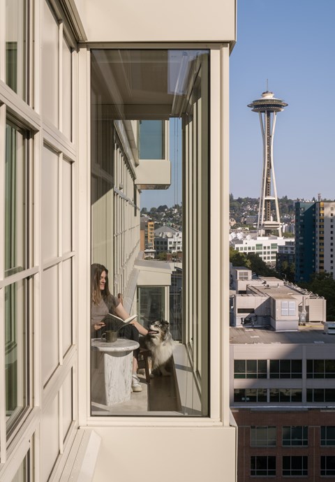 A woman is sitting at a table with her dog in a room with a view of the Space Needle.