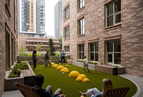 A group of people are sitting and standing on a grassy area between two buildings.