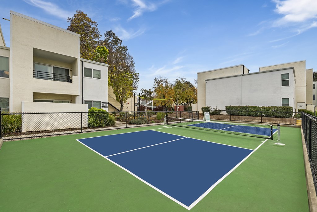 A tennis court is surrounded by apartment buildings.