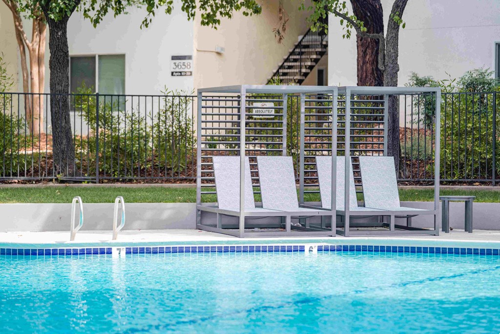 a row of white lounge chairs by a pool with a building in the background