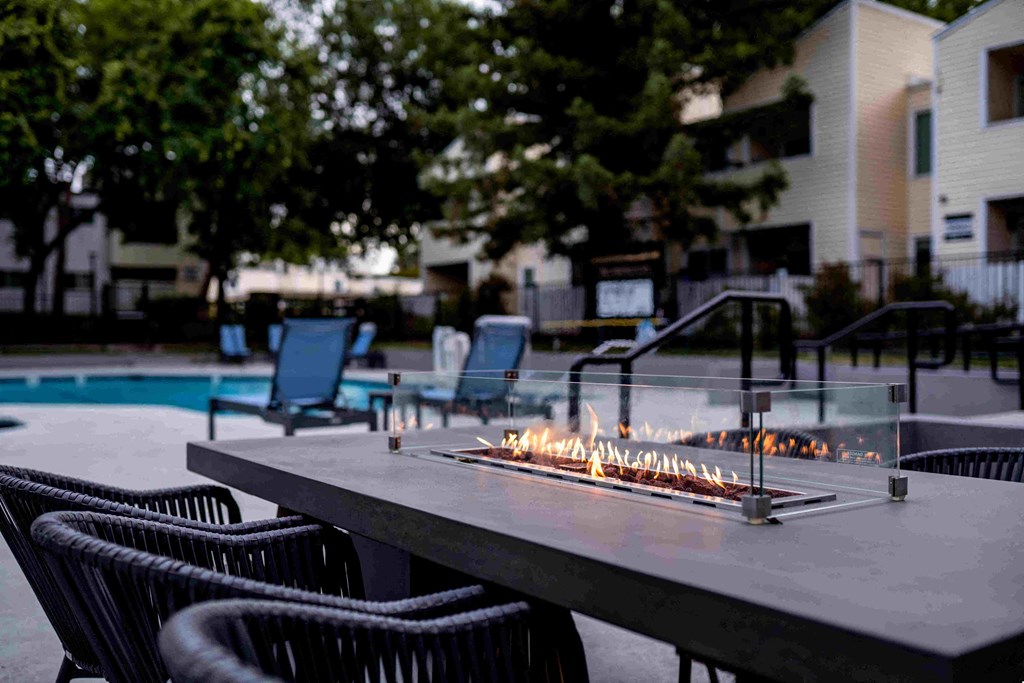 a patio with a table and chairs and a fire pit in front of a pool
