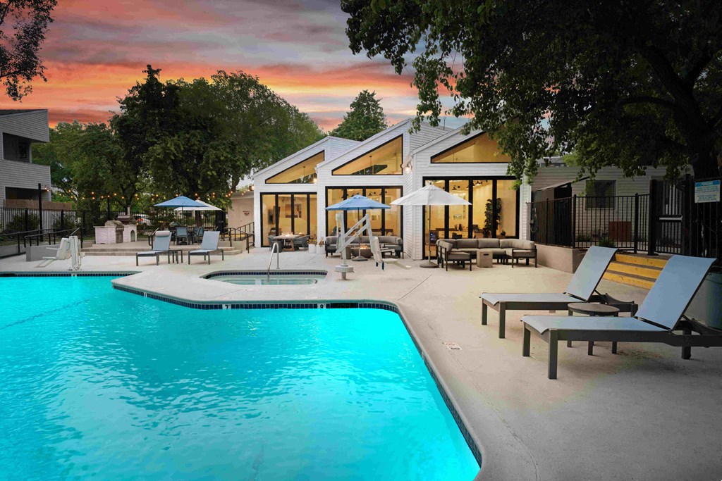 a swimming pool with lounge chairs and umbrellas in front of a house