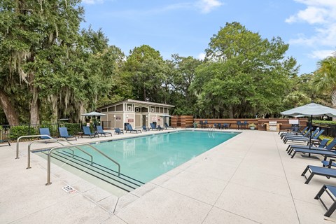 A pool surrounded by trees and chairs.