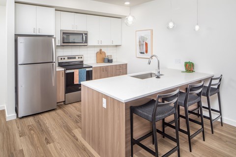a kitchen with an island with three stools and a stainless steel refrigerator