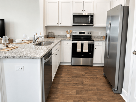 A kitchen with a stainless steel refrigerator, a microwave above the stove, and a sink with a granite countertop.