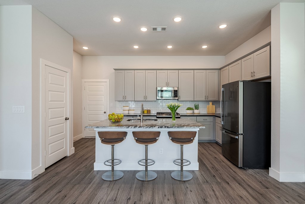 a kitchen with a island with three stools and a black refrigerator