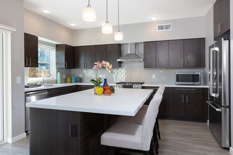 a kitchen with a large island with two stools and a stainless steel refrigerator