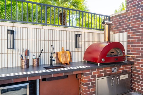 A red pizza oven is on a brick wall.