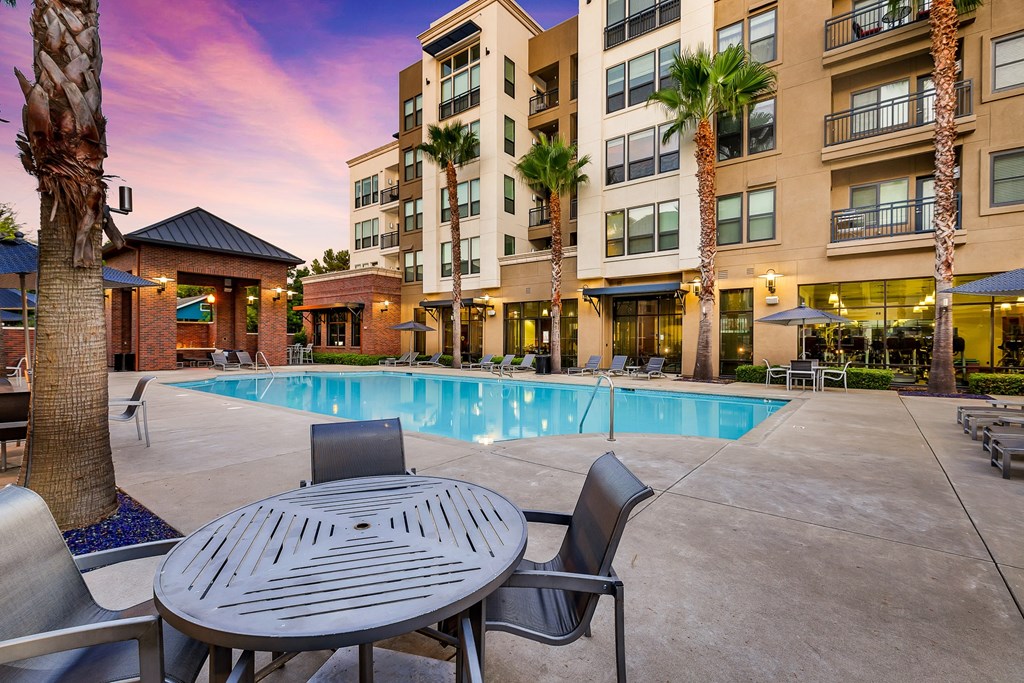 a swimming pool with a table and chairs in front of an apartment building