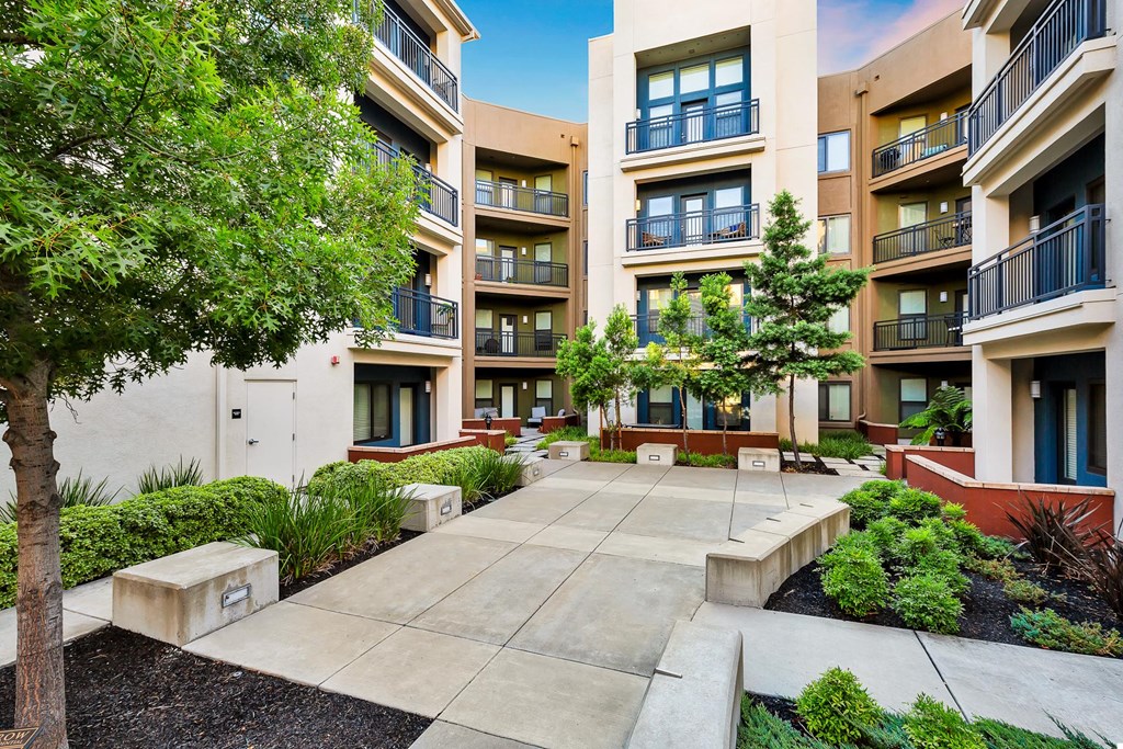 a courtyard with benches and trees in front of an apartment building
