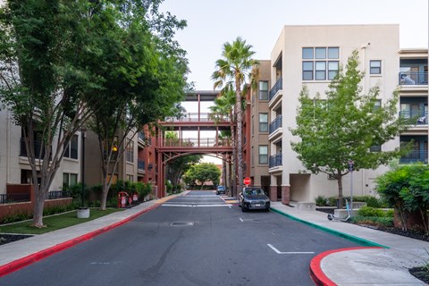 A street with a car driving down it and apartment buildings on either side.
