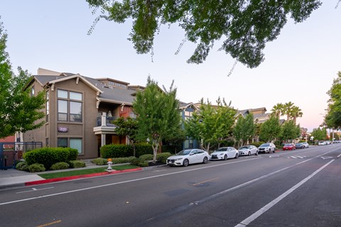 A street with cars parked on the side and apartment buildings in the background.