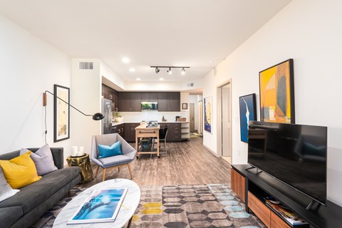 A living room with a grey couch, a blue chair, a coffee table with a painting on it, and a television on a wooden stand.