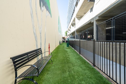 A black bench sits on a green lawn next to a wall with a painting of a tree.