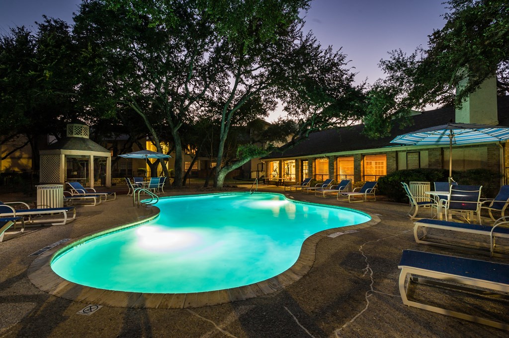 a night view of a pool with lounge chairs and umbrellas
