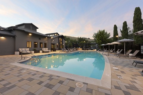 A swimming pool surrounded by a tiled patio and lounge chairs.