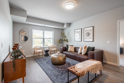 A living room with a brown leather couch, a round coffee table, and a large window.