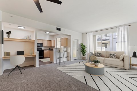 A modern living room with a grey carpet and a white ceiling fan.