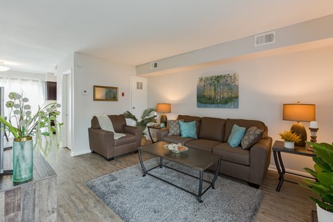 A living room with a brown couch and a glass vase with plants in it.