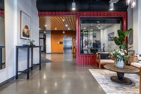 A modern office lobby with a red accent wall and a glass door leading to another room.
