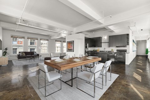 a dining area with a wooden table and chairs and a kitchen in the background