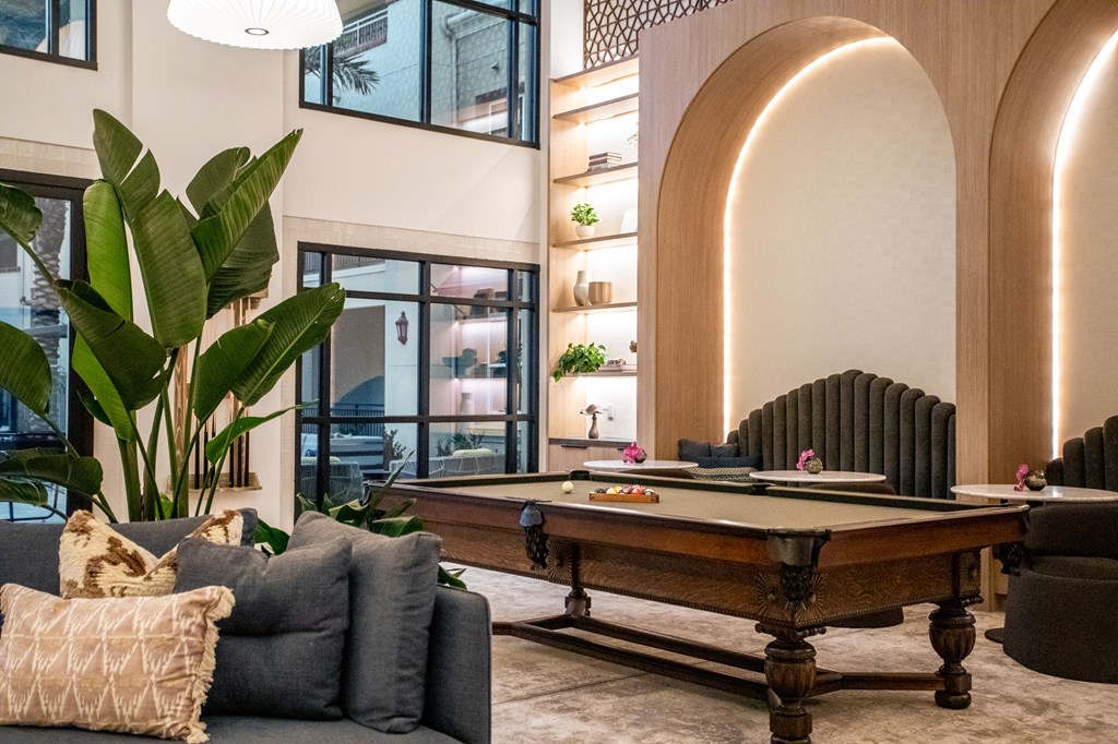 A pool table is in the middle of a living room with a couch and a plant.