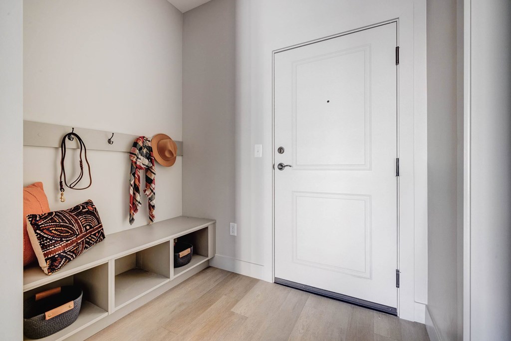 A white door is closed in a room with a bench and a hat hanging on the wall.