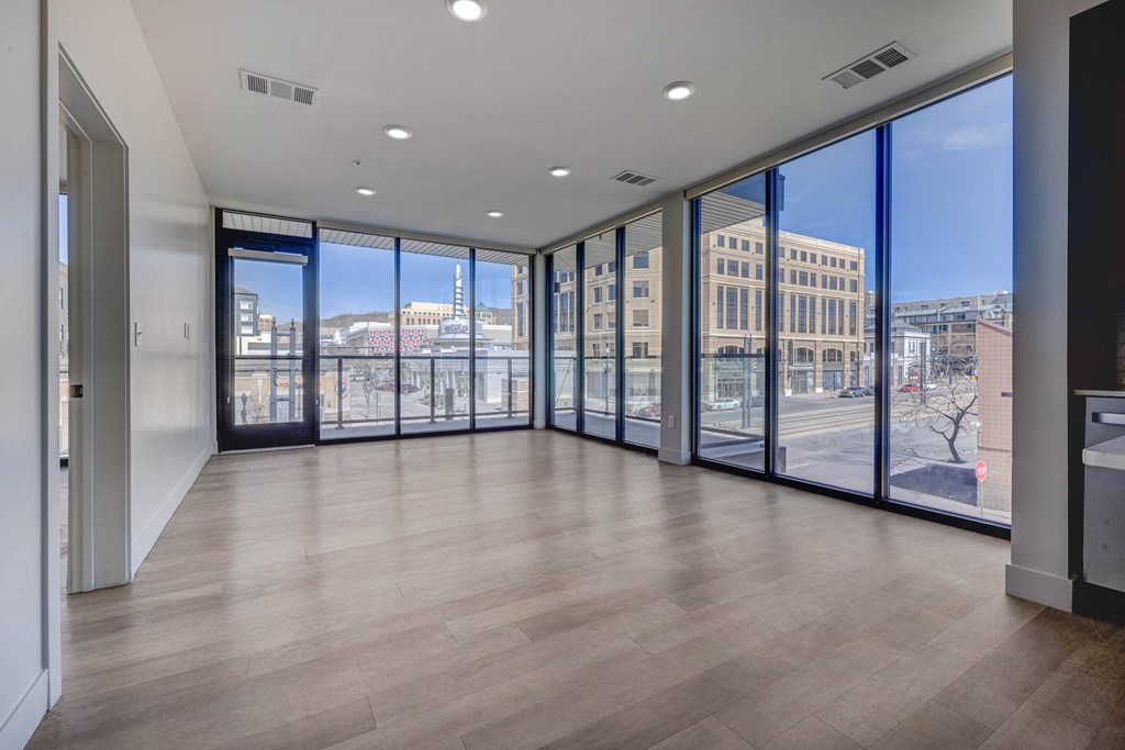 A spacious room with wooden floors and large windows overlooking a cityscape.