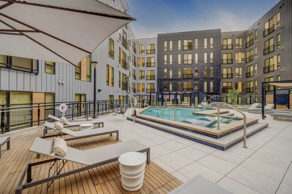 A modern pool area with a wooden deck and sun loungers.