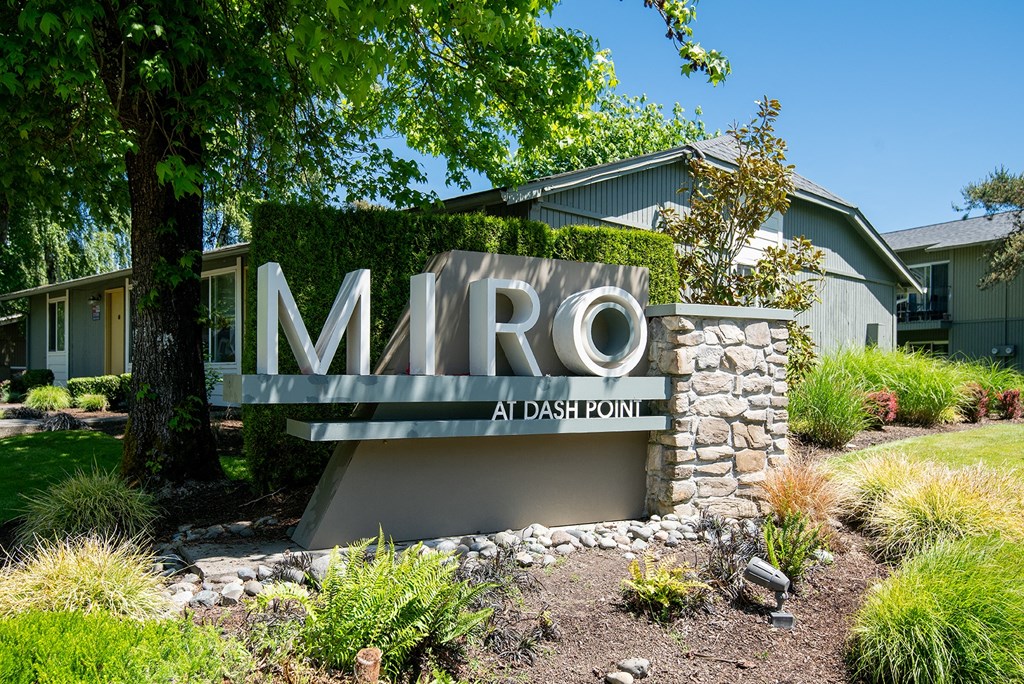 a sign in front of a house with a lawn and trees