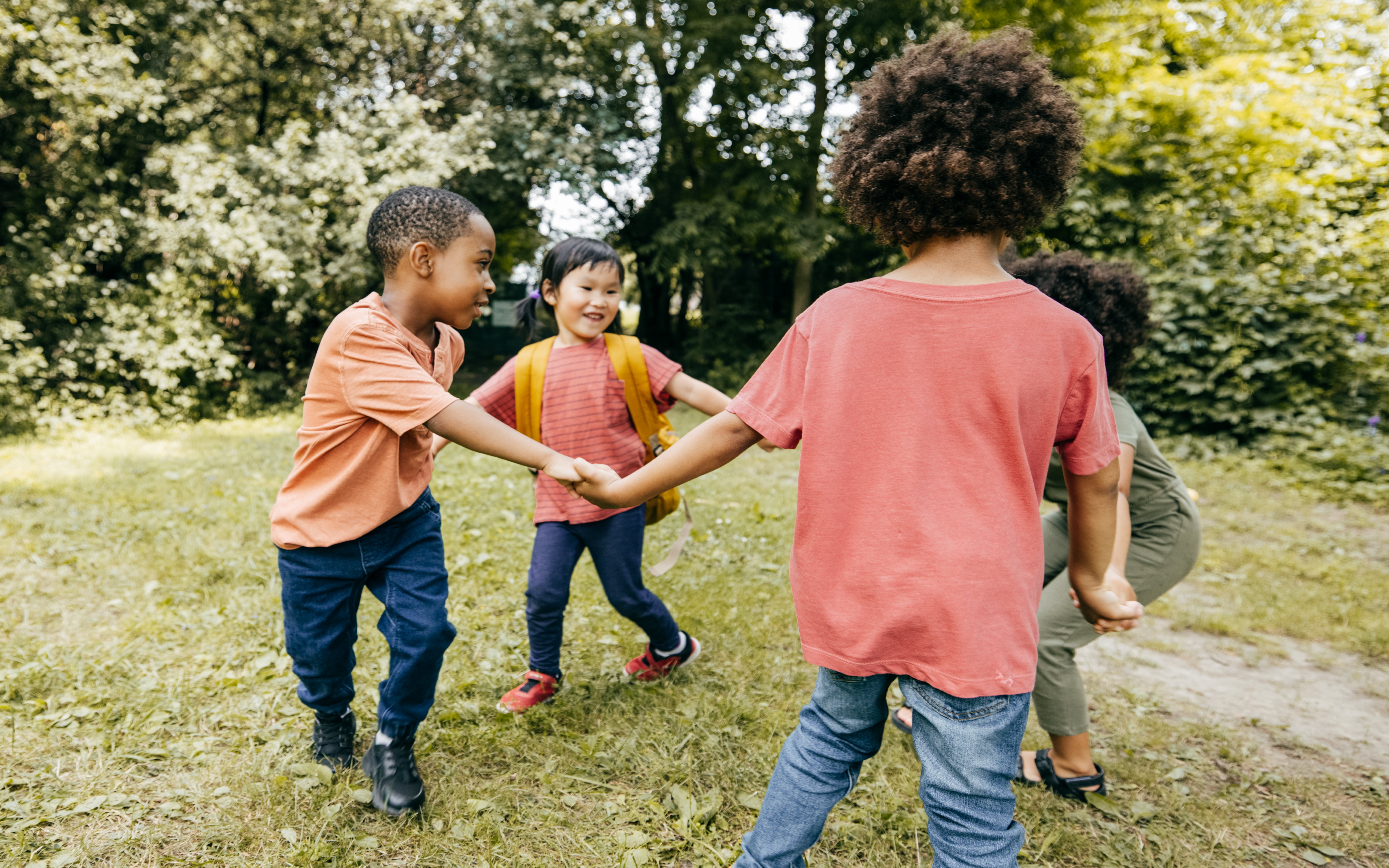 Three children are playing tug of war in a grassy area.