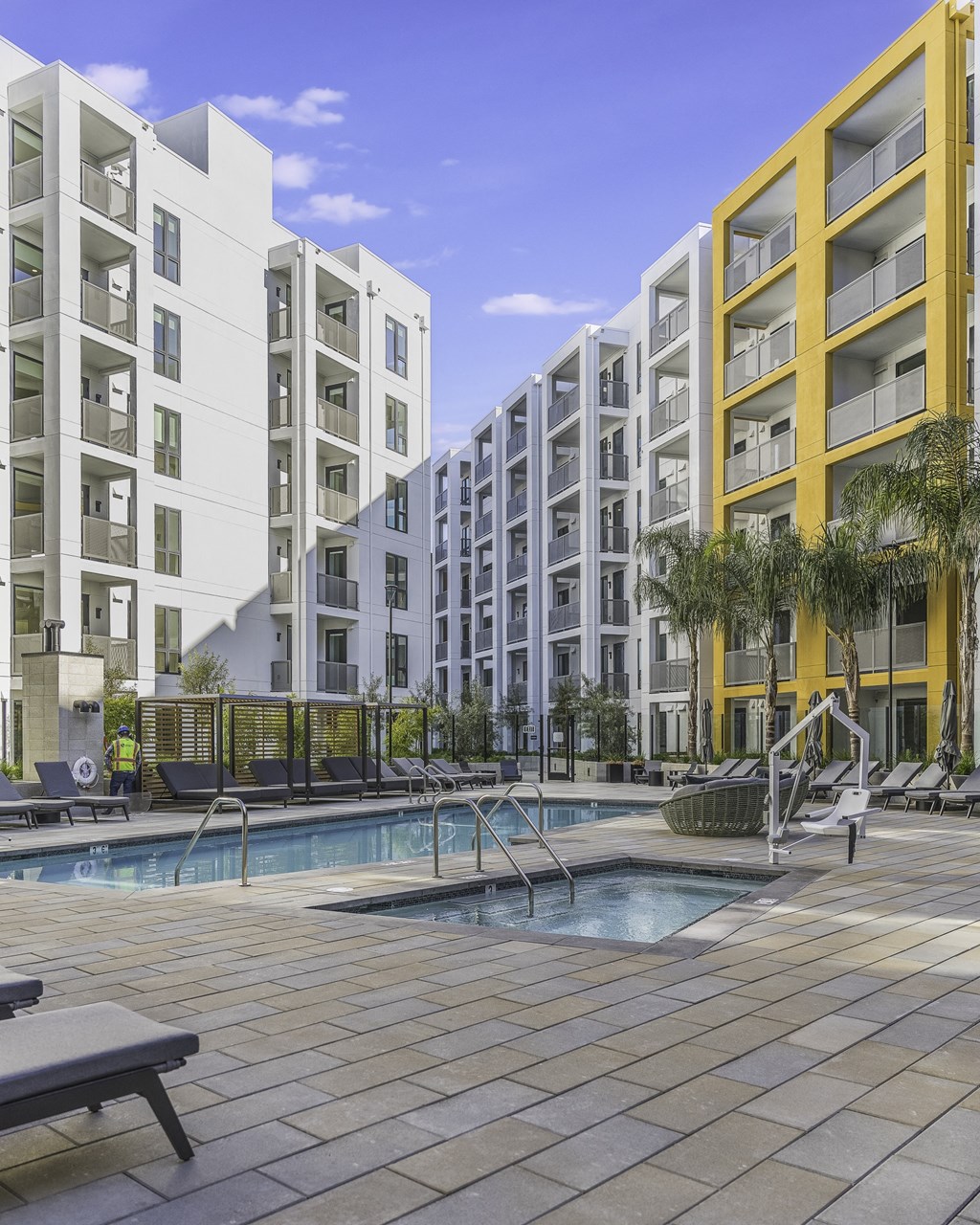 A pool area with a bench and a tree in front of a yellow building.