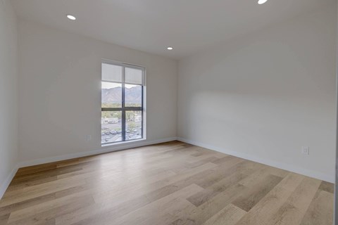 A spacious room with wooden flooring and a large window.