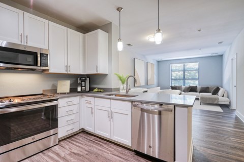 an open kitchen and living room with white cabinets and stainless steel appliances